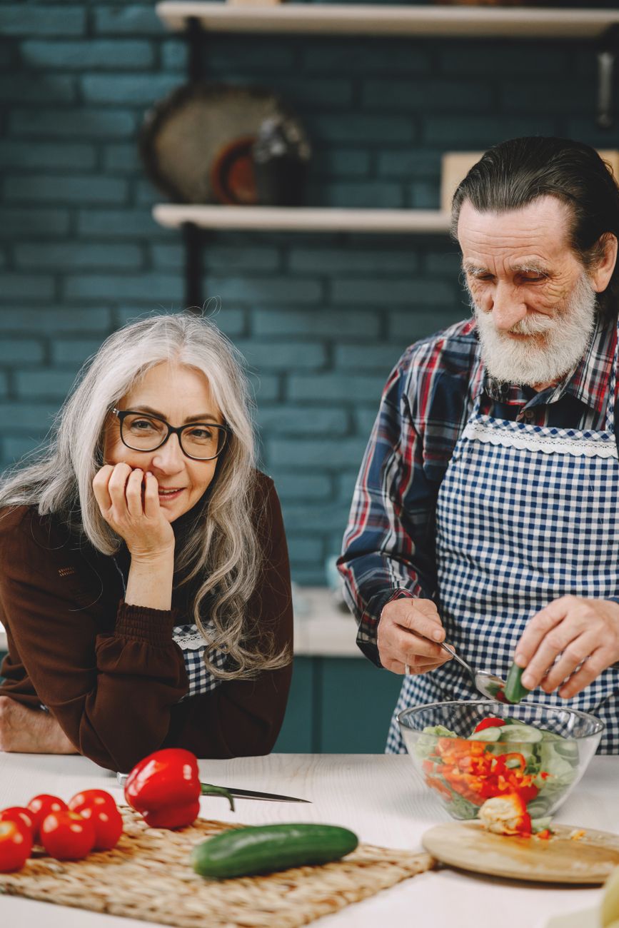 Caregiver preparing fresh healthy meal for older elderly gentleman in apartment